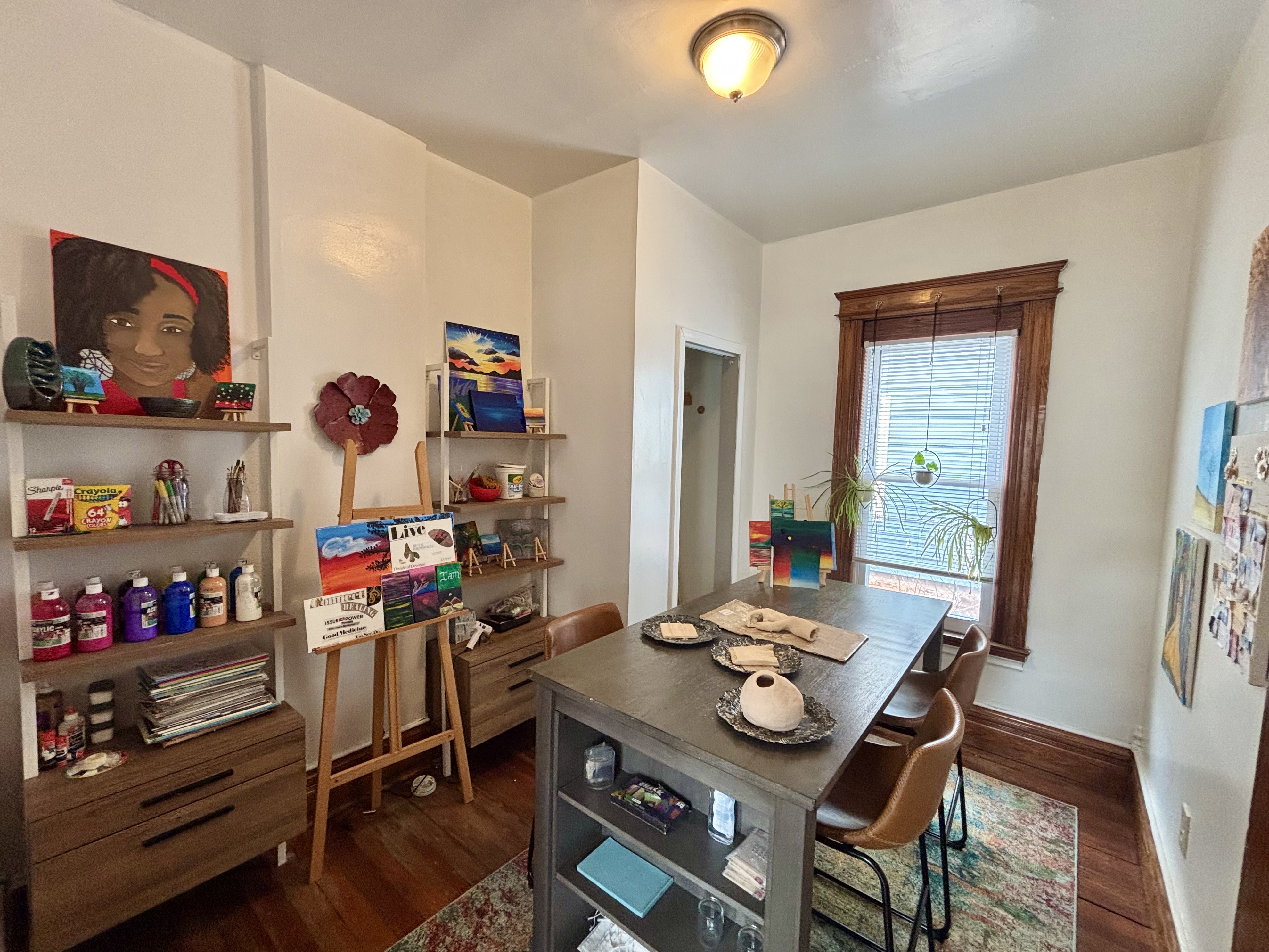 An art studio with a table, chairs, and paintings on the wall.